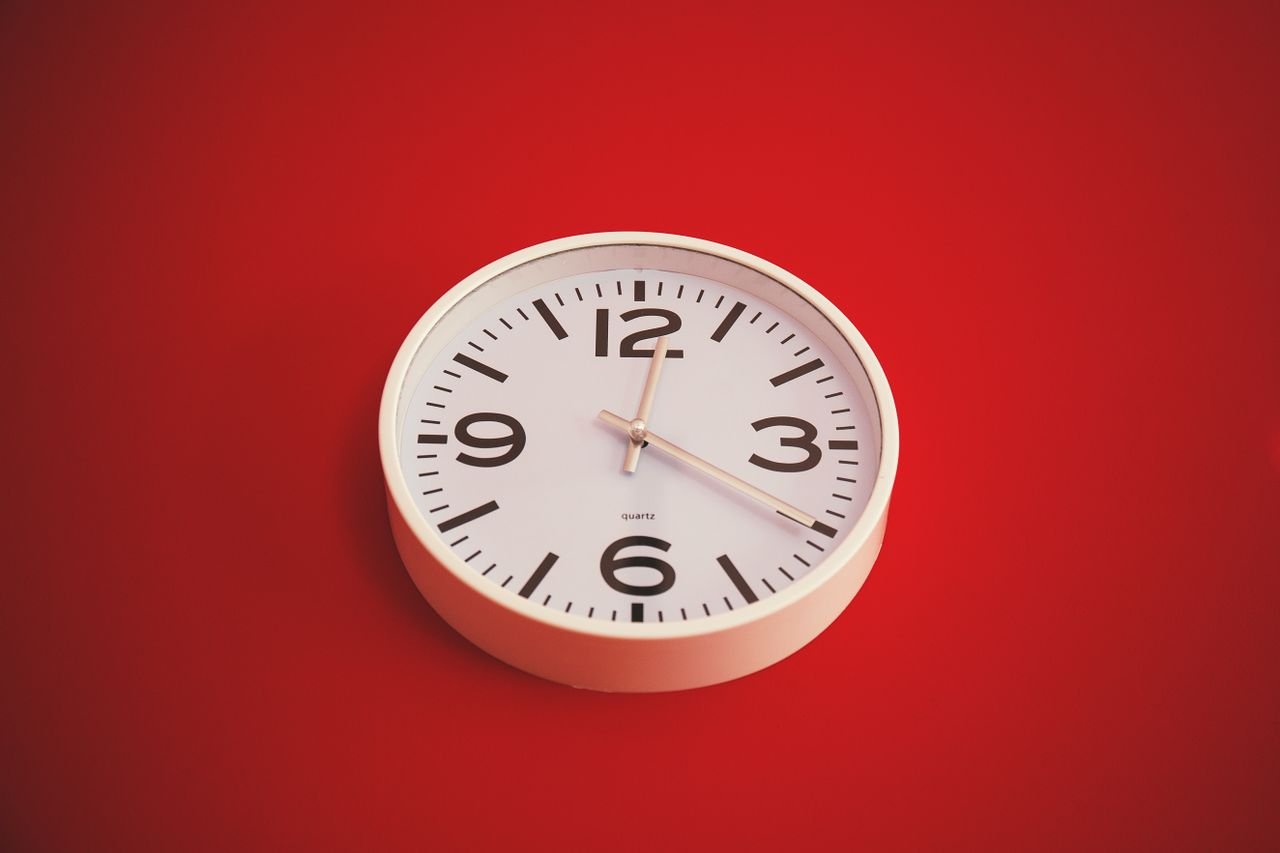 Services Minimalist round wall clock with a white face on a vibrant red background. Time marked as three o'clock.