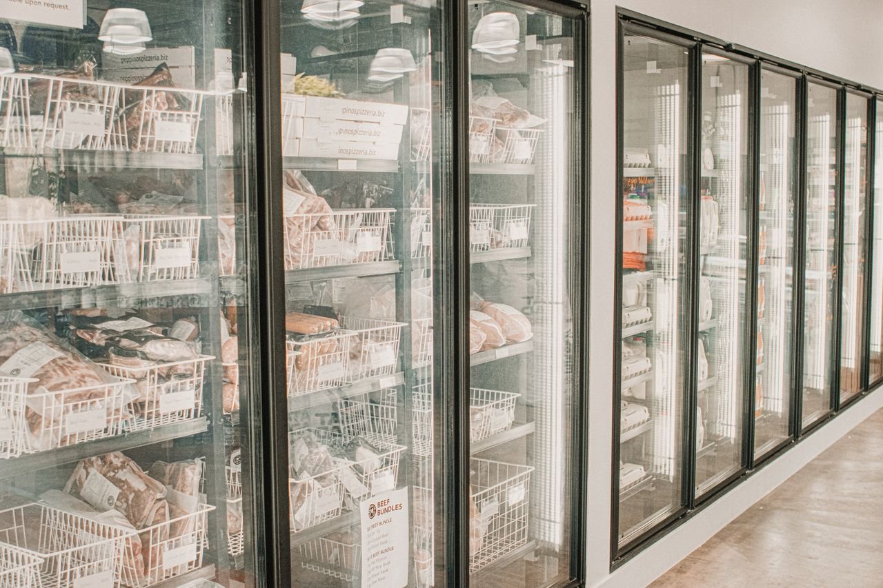 Home Frozen meats in a retail freezer with transparent doors and organized sections.