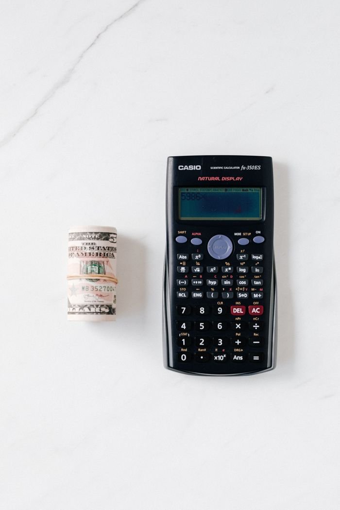 Home Top view of roll of paper money tied with rubbed band near rectangular calculator with numbers and symbols on marble surface
